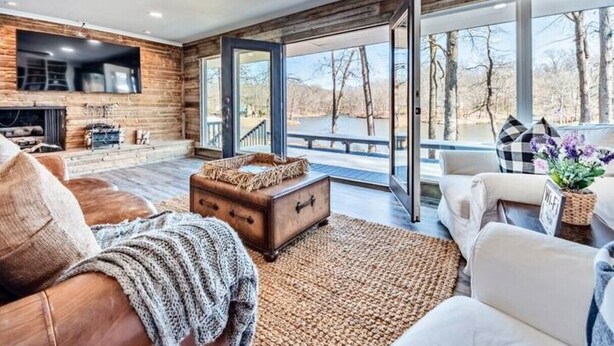 A modern living room with a fireplace, leather sofa, and a view of a lake.