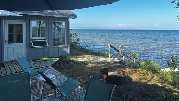Ett hus vid kusten med en terrass som vetter mot havet, med utomhusmöbler och en eldstad.
