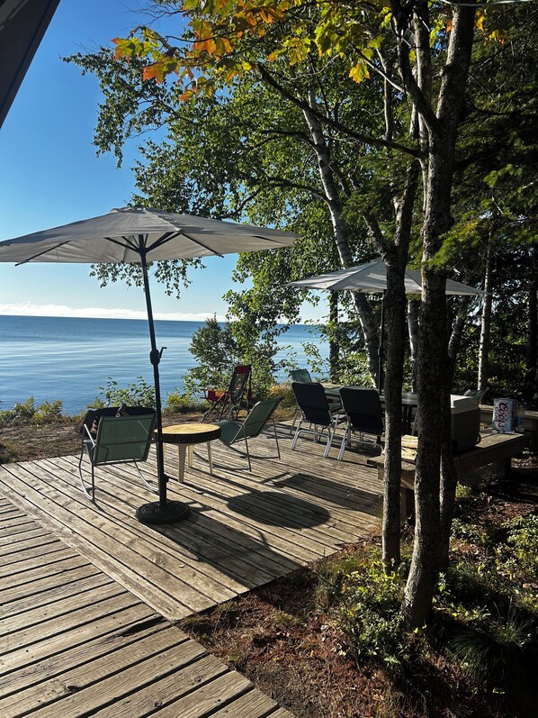 A wooden deck with outdoor furniture, including chairs and a table, overlooking a body of water.
