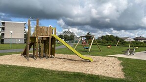 A playground with a slide, swings, and a climbing structure. - Family apartment for 6 people (De Haan)
