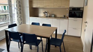 A modern kitchen with white cabinets, a wooden countertop, and a dining area with a table and chairs. - Family apartment for 6 people (De Haan)