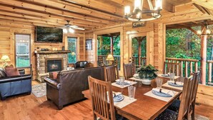 L’intérieur d’un chalet en bois comprend une cheminée, des sièges en cuir, une table à manger et un balcon offrant une vue sur la forêt.