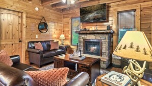 L’intérieur d’un chalet confortable, avec une cheminée, des meubles en cuir et un ventilateur de plafond.
