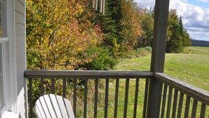 A wooden deck with a white Adirondack chair and a small table. - Black Bear Pond Cabins (Patten)