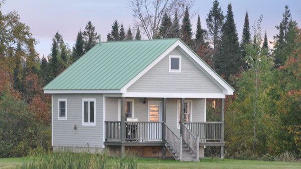 A two-story lodge with a green roof, a front porch, and a staircase leading to the entrance. - Black Bear Pond Cabins (Patten)