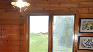 A wooden-paneled room with a window, two wooden chairs, a table with a pink tablecloth, and a bowl of fruit. - Black Bear Pond Cabins (Patten)