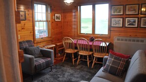 A cozy cabin interior with wooden walls, a dining table with chairs, a sofa, and a fireplace. - Black Bear Pond Cabins (Patten)