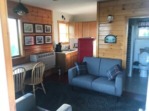 A cozy cabin interior with a dining area, a sofa, a red refrigerator, and a kitchen with wooden cabinets. - Black Bear Pond Cabins (Patten)