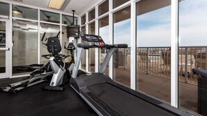 Un gimnasio con caminadora, elíptica y bicicleta estática, ventanas amplias que dan a una piscina y zona exterior.