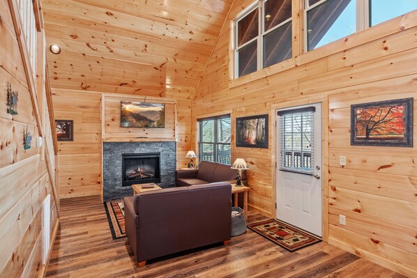 A cozy cabin interior with a fireplace, wooden walls, a sofa, and a door with a window.
