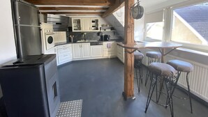 Cozinha com armários brancos, geladeira de aço inoxidável, teto com vigas de madeira e janela com vista para o exterior.