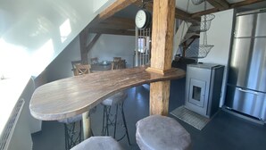 Cozinha com mesa de madeira, banquetas de bar, luminária pendente, relógio e geladeira de aço inoxidável.