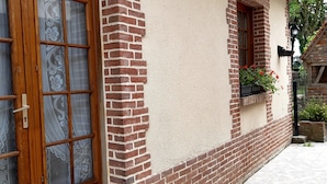 Een gebouw met een bakstenen gevel, een groot raam met houten kader en een klein raam met bloembak.