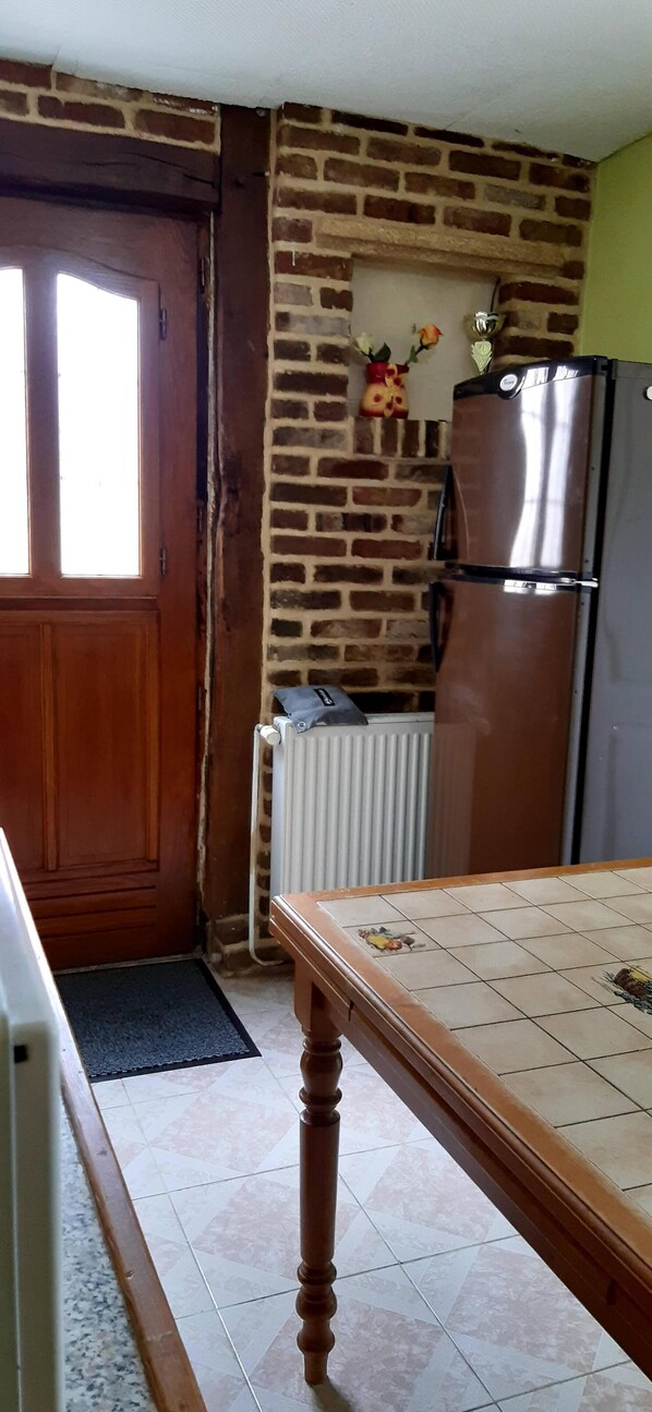 A kitchen with a brick wall, a wooden door, a refrigerator, and a tiled floor. - Le Gîte de la Roseraie des Bois Free Parking (Aubermesnil-aux-Érables)