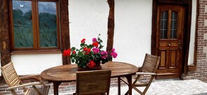 A wooden table with chairs and a potted plant with red and pink flowers. - Le Gîte de la Roseraie des Bois Free Parking (Aubermesnil-aux-Érables)