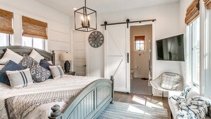 Ein Schlafzimmer mit einem Bett, einem Sessel, einem Fernseher und einer Tür zu einem anderen Raum.