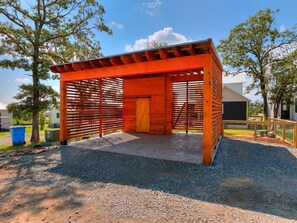 A wooden structure with a slatted roof and a central door, surrounded by gravel and trees.