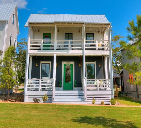 A two-story house with a front porch, a green door, and a balcony on the upper floor.