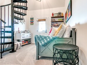 A room with a spiral staircase, a bed with a blue blanket, a small round table, and a bookshelf with books and decorative items.