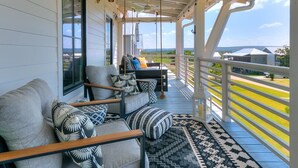 Eine überdachte Veranda mit einer Couch und Sesseln, einem gemusterten Teppich und Blick auf eine Wohngegend.