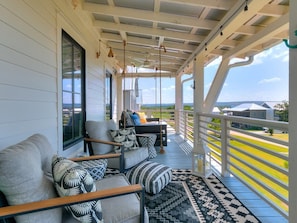 Eine überdachte Veranda mit einer Couch und Stühlen, Blick auf die Landschaft und einem Geländer.