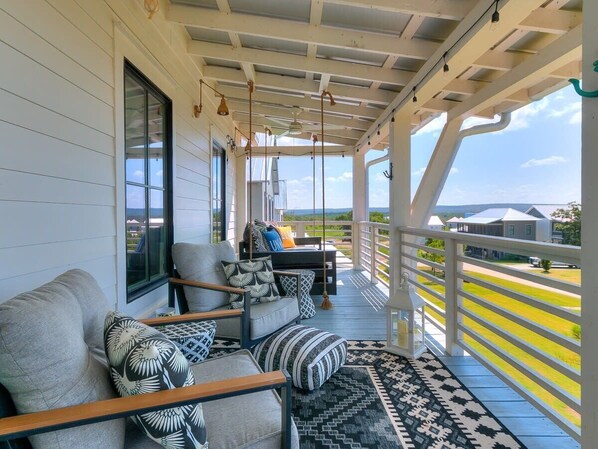 A covered porch with a sofa and chairs, a view of the landscape, and a railing.
