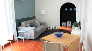 A modern living room with a grey sofa, a small blue table, and a white chair. - Alley house historical center (Catania)