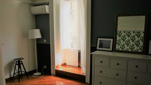 A room with a bed, a desk, a chair, a dresser, a mirror, and a door leading to a balcony. - Alley house historical center (Catania)