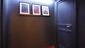 A hallway with a dark wall, a door with a handle, and three framed pictures on the wall. - Alley house historical center (Catania)