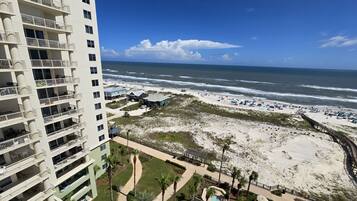 A high-rise hotel with multiple balconies overlooking a beach with umbrellas and a boardwalk.