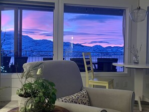 A living room with a large window overlooking a snowy landscape during sunset. - Sage View Suites (Peachland)