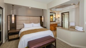 Une chambre d’hôtel avec un grand lit, une banquette, une salle de bain avec un miroir et une coiffeuse.