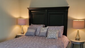 A neatly made bed with a patterned bedspread, flanked by two bedside tables with lamps and decorative vases. - Spacious apartment, deep in the woods, with private entrance and deck (Cleveland)