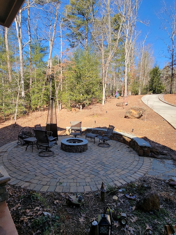 A circular outdoor seating area with a fire pit, surrounded by stone walls and furnished with chairs and tables.