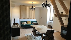 Un espacio habitable moderno con zona de comedor, un sofá con cojines, una araña y un revestimiento de pared de madera.