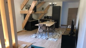 Una cocina moderna con vigas de madera, un comedor con sillas estampadas y un mueble negro para televisor.