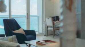 Une pièce avec une grande fenêtre, une chaise, une table et un bureau avec un ordinateur.