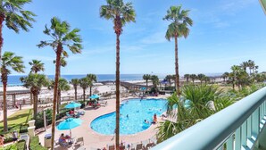 Zona de piscina con palmeras, vista a la playa y cielo despejado.