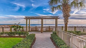 Un paseo techado que conduce a una playa con una pérgola, palmeras y vistas al mar.