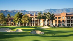 A golf course with bunkers and palm trees, a building with balconies, and mountains in the background. - Marriott Shadow Ridge - Studio Villa with King bed (Palm Desert)