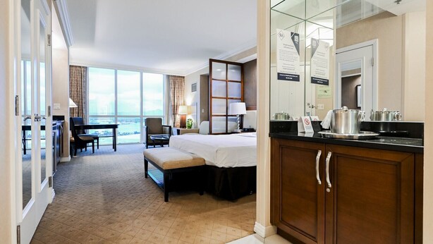 A hotel room with a bed, a desk, a chair, a view of the city, and a kitchenette. - SVS: MGM 2BR, Mtn View, Balcony & 3 Baths (Las Vegas)