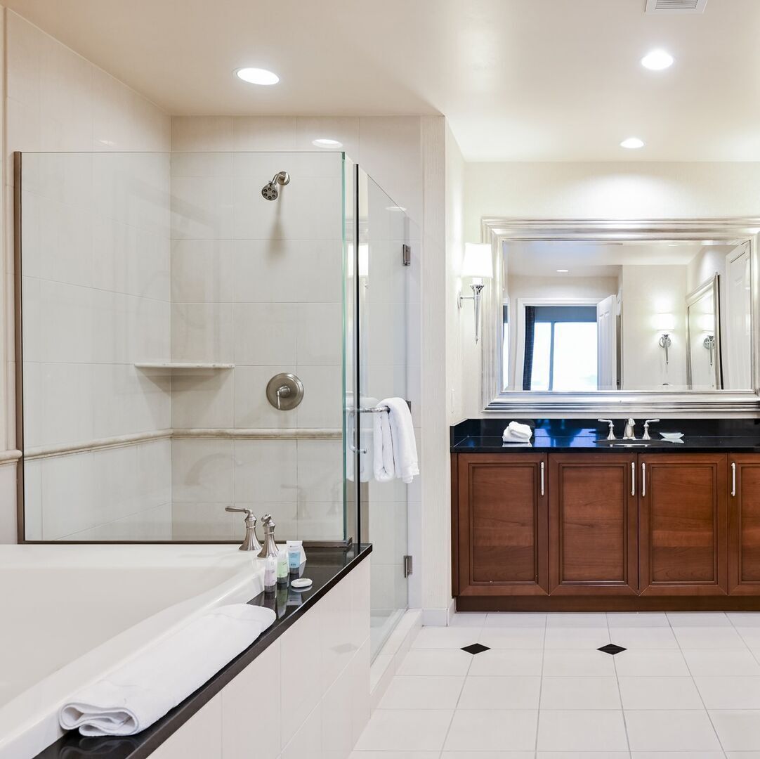 A modern bathroom with a glass-enclosed shower, a large mirror, and a black countertop with toiletries.
