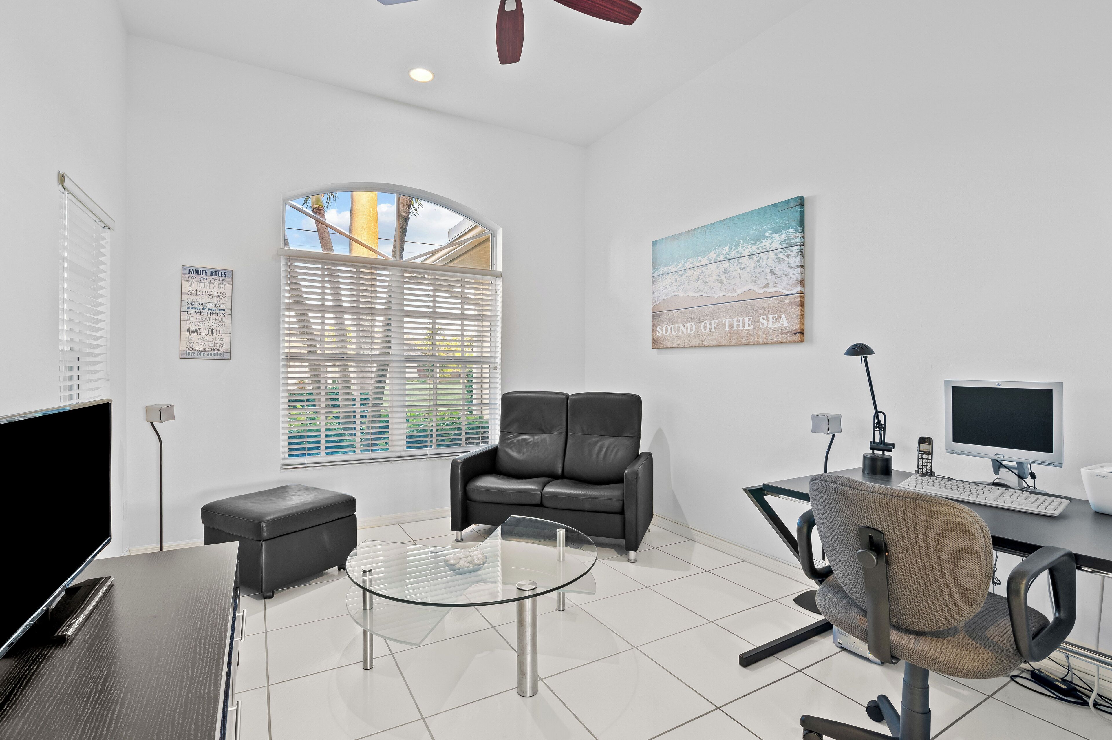 A modern office with a glass table, leather sofa, and a desk with a computer.