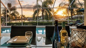 A table set for dining with a view of the sunset over a pool and palm trees. - Intervillas Florida - Villa Magic Summer (Cape Coral)