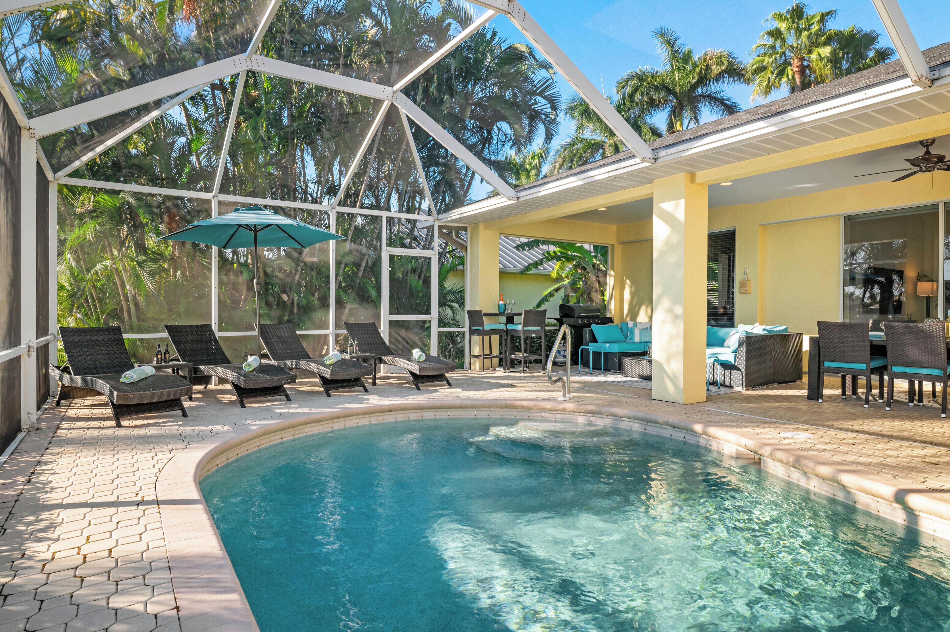 A pool area with lounge chairs, a table, and umbrellas.