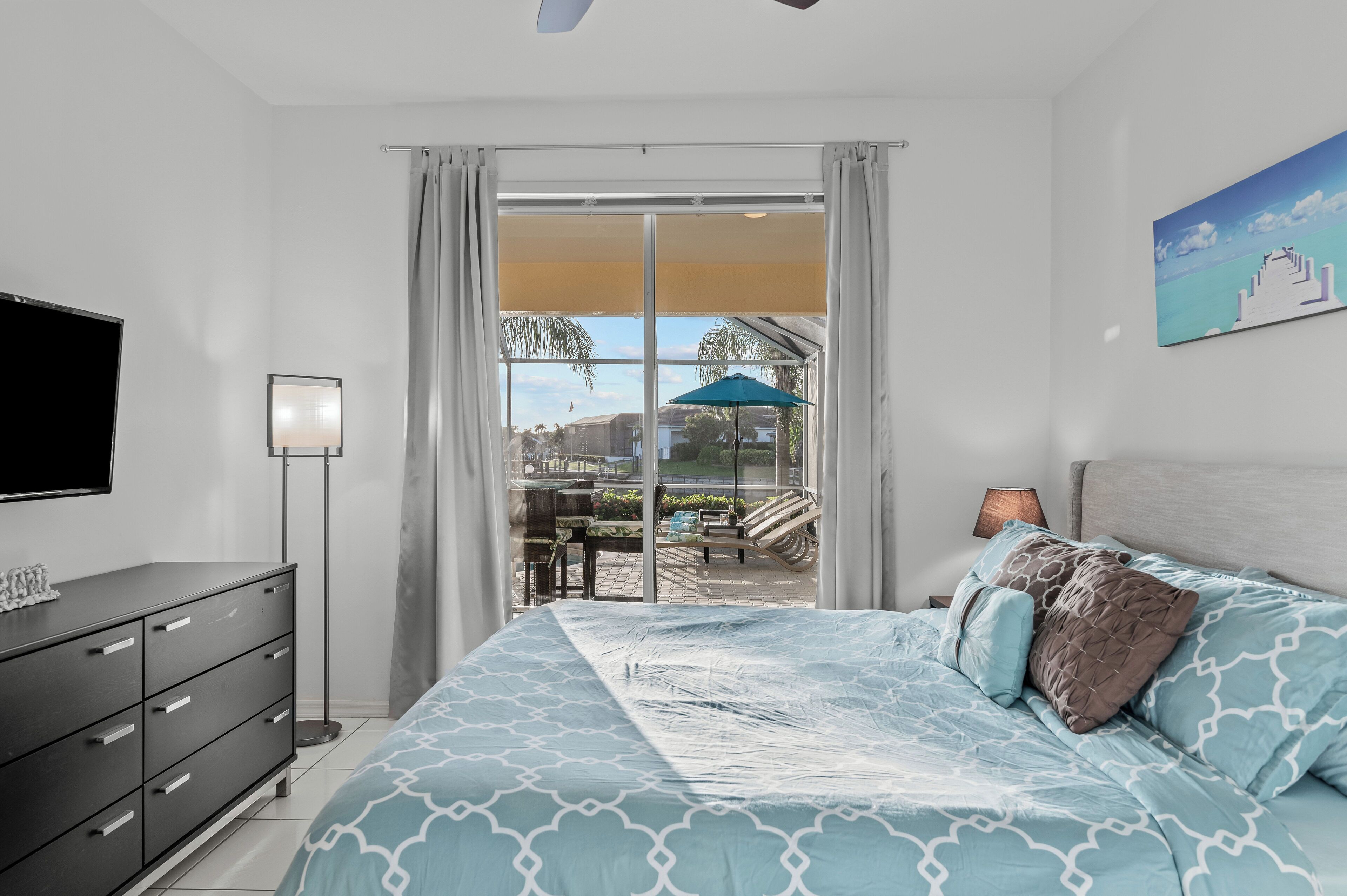 A bedroom with a bed, a TV, a desk, and a view of the outdoors.