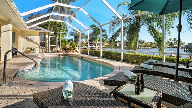 A pool area with a glass ceiling, lounge chairs, and a view of a body of water. - Intervillas Florida - Villa Magic Summer (Cape Coral)