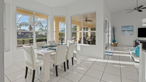 A bright, spacious dining area with a large table and chairs, large windows offering views of the outdoors, and a ceiling fan. - Intervillas Florida - Villa Magic Summer (Cape Coral)