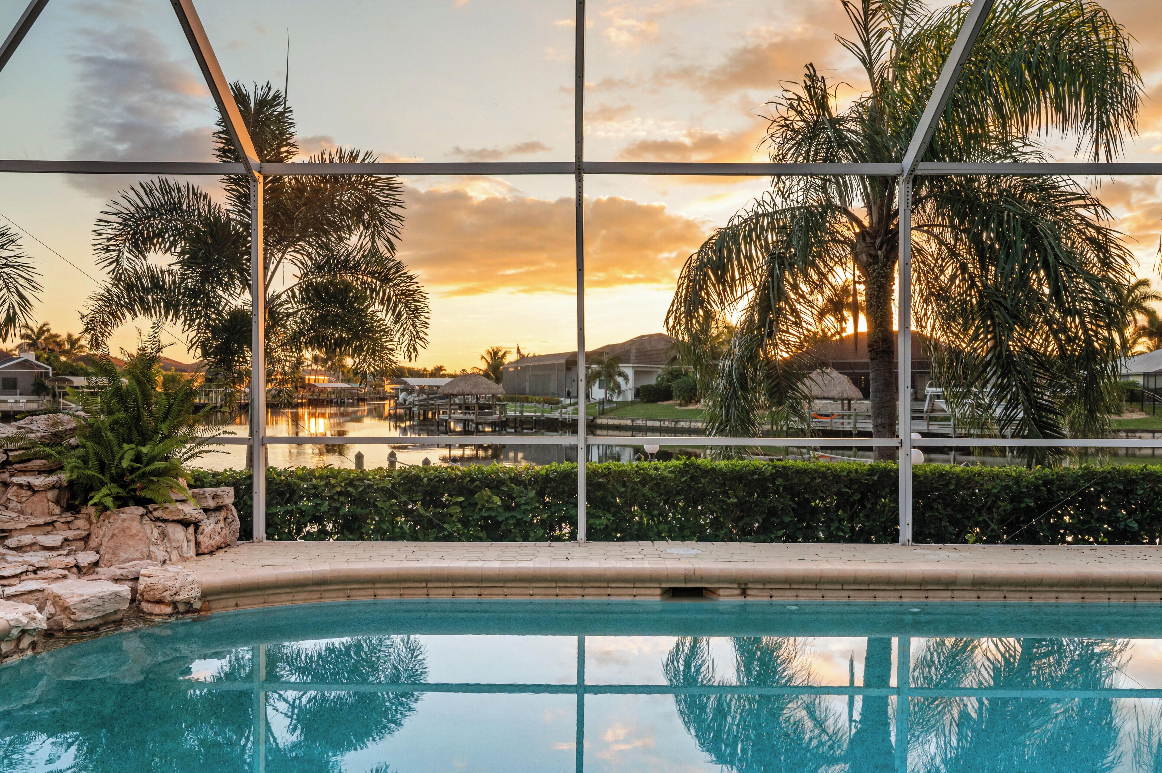 A pool with a view of palm trees and a sunset.