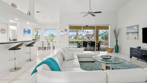 A modern living room with a white sofa, a glass coffee table, and a bar area with stools. - Intervillas Florida - Villa Magic Summer (Cape Coral)
